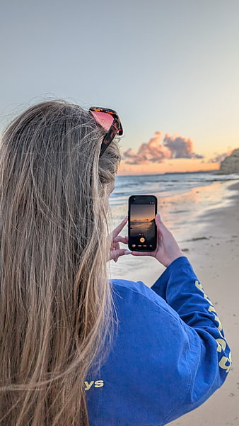 Woman photographing beach sunset with smartphone