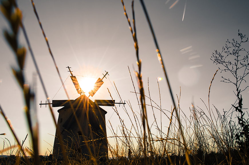 Silhouette of old windmill at sunset through tall grass