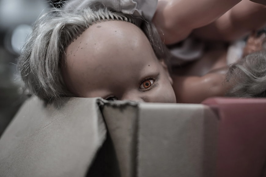 Close-up of creepy porcelain doll peeking from cardboard box