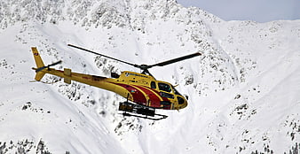 Yellow rescue helicopter flying over snowy Swiss Alps