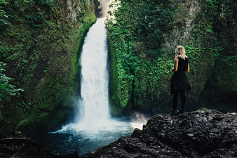 Woman standing on rock overlooking lush green waterfall
