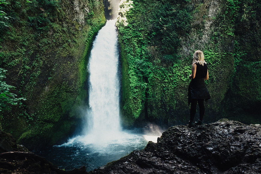 Woman standing on rock overlooking lush green waterfall