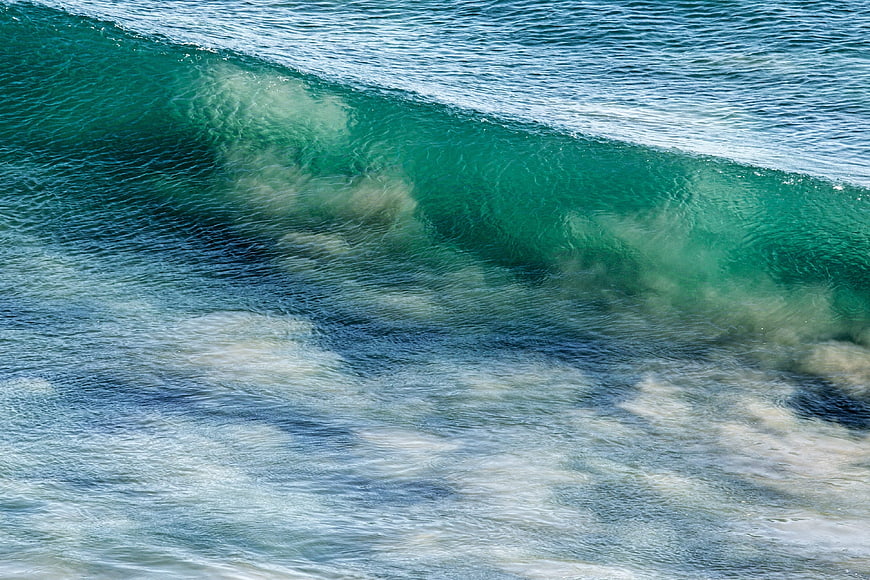 Aerial view of turquoise ocean wave crashing with white foam