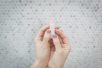 Hands holding pink lip balm against mosaic background