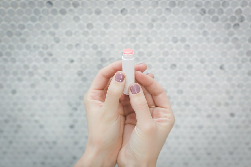 Hands holding pink lip balm against mosaic background