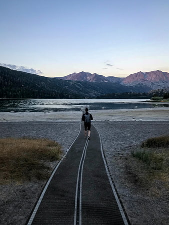 Hiker walking on boardwalk path towards mountains at sunset