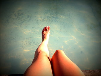 Relaxing legs in clear pool water with sunlight caustics