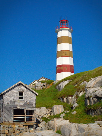 Striped Lighthouse on Rocky Coastal Hill with Weathered Shed