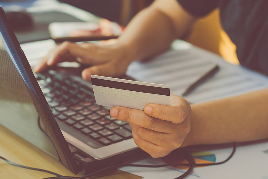 Person holding credit card while typing on laptop for online shopping