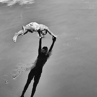 Black and white photo of a man jumping to touch his reflection in water