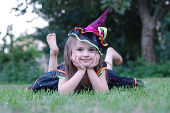 Smiling young girl in witch costume lying on grass
