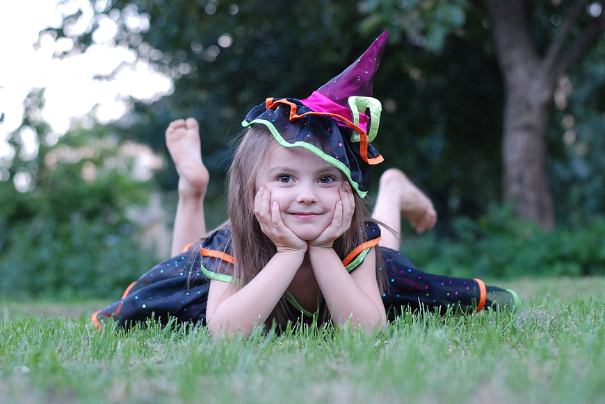 Smiling young girl in witch costume lying on grass