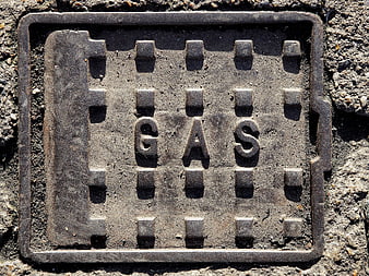 Close-up of weathered metal gas utility cover embedded in asphalt