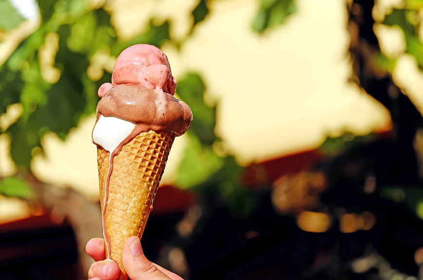 Hand holding melting triple scoop ice cream cone outdoors