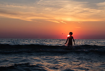 Silhouette of Boy Splashing in Ocean at Sunset