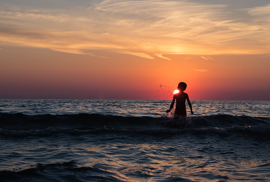 Silhouette of Boy Splashing in Ocean at Sunset