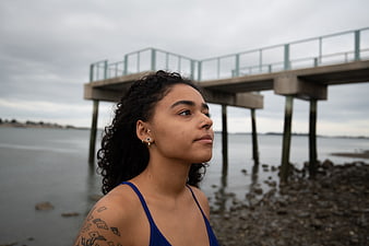 Contemplative woman with tattoos standing by ocean pier