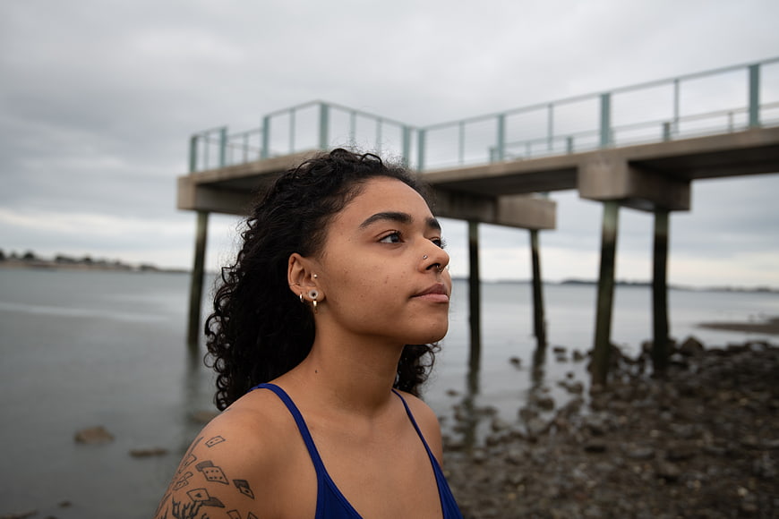 Contemplative woman with tattoos standing by ocean pier