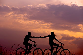 Silhouette of couple holding hands on bicycles at sunset