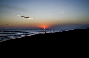 Silhouette of lone figure on beach at sunset