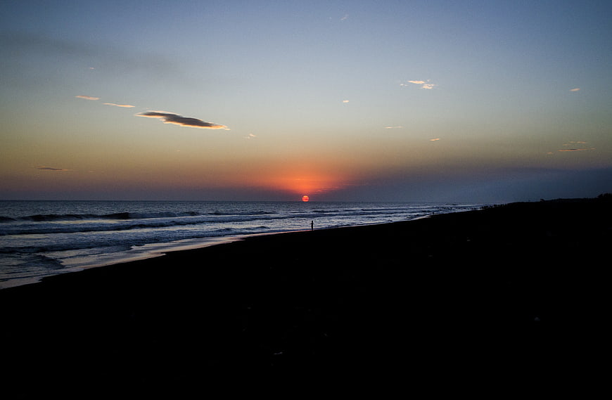 Silhouette of lone figure on beach at sunset