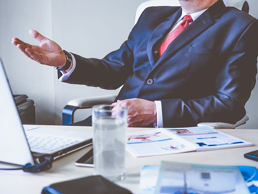 Businessman gesturing at office desk with laptop and documents
