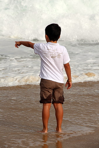 Boy standing on beach pointing at ocean waves