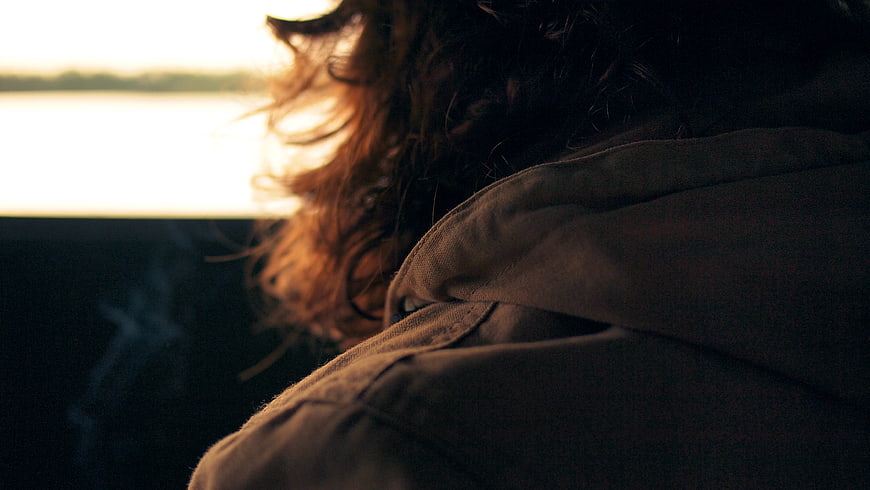 Close-up of man with curly hair in hood looking out window