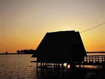 Silhouette of wooden house on stilts at sunset over water