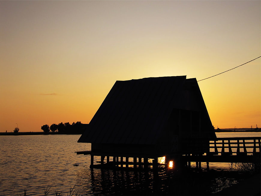 Silhouette of wooden house on stilts at sunset over water