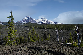 Snow-capped mountains rising above a rugged volcanic lava field landscape