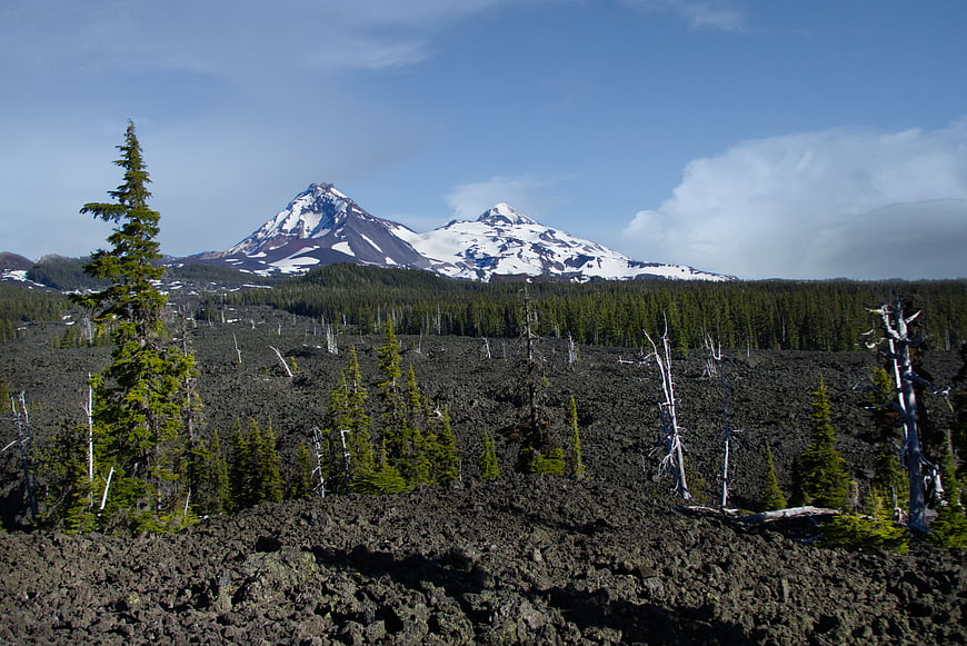 Snow-capped mountains rising above a rugged volcanic lava field landscape