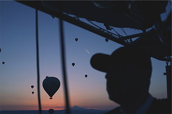 Silhouette of man in hot air balloon basket at dusk