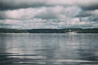 Lone sailboat on calm water under dramatic cloudy sky