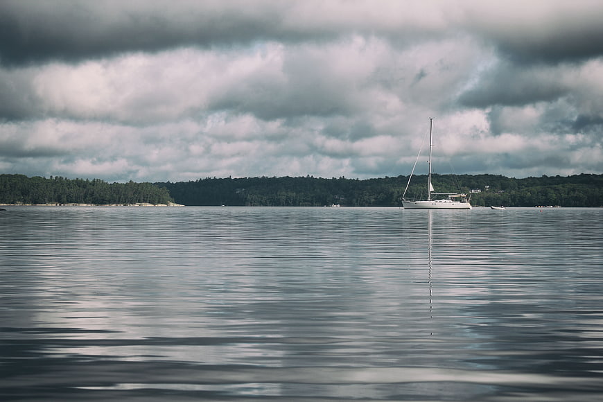 Lone sailboat on calm water under dramatic cloudy sky