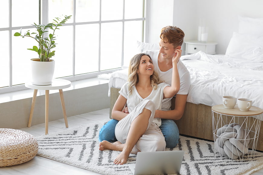 Happy couple relaxing on bedroom floor with laptop