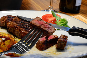 Close-up of sliced medium-rare steak with roasted potatoes and tomato garnish