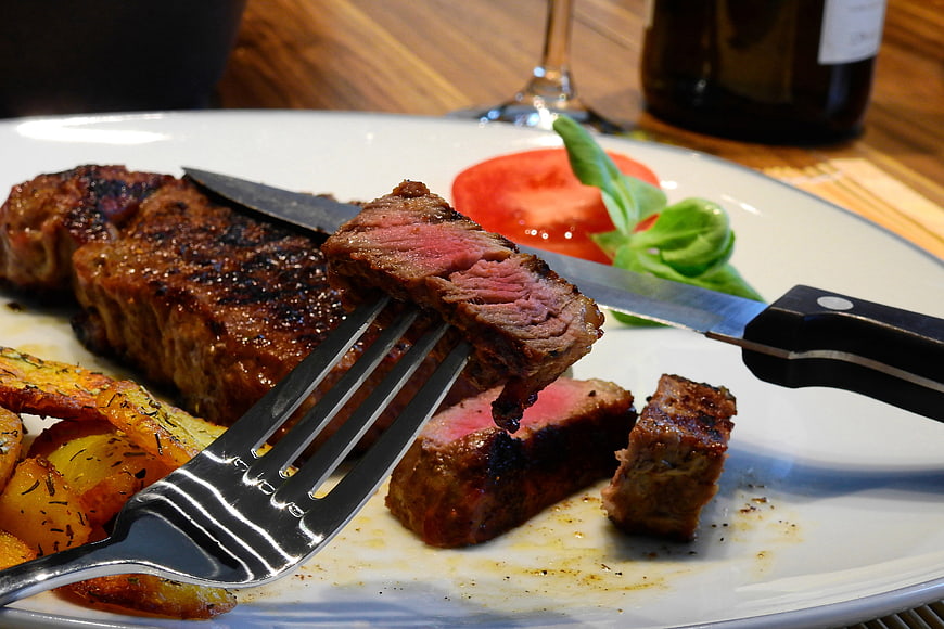 Close-up of sliced medium-rare steak with roasted potatoes and tomato garnish