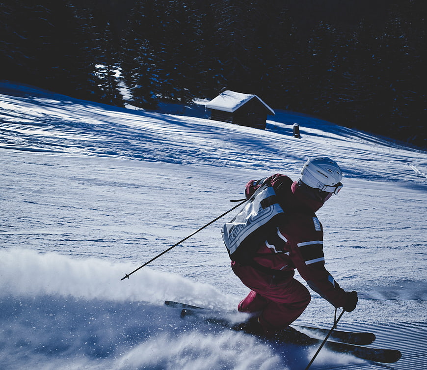 Skier carving turn on snowy slope with cabin background
