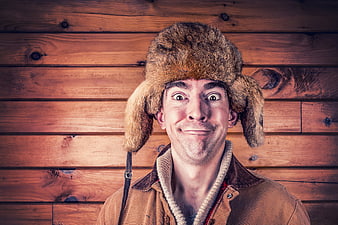 Man in Fur Hat Making Funny Face Against Wood Background