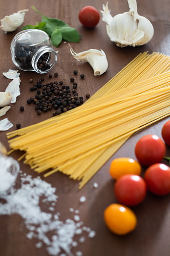 Uncooked spaghetti, cherry tomatoes, garlic, and spices on wooden table