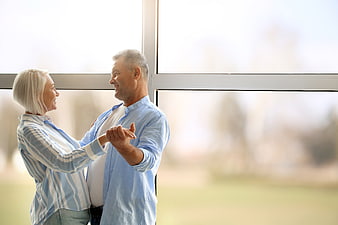 Happy senior couple dancing indoors by window