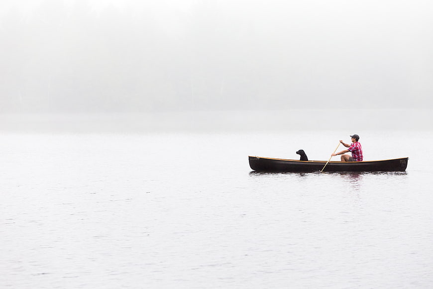 Man and Dog Paddling Canoe on Misty Lake