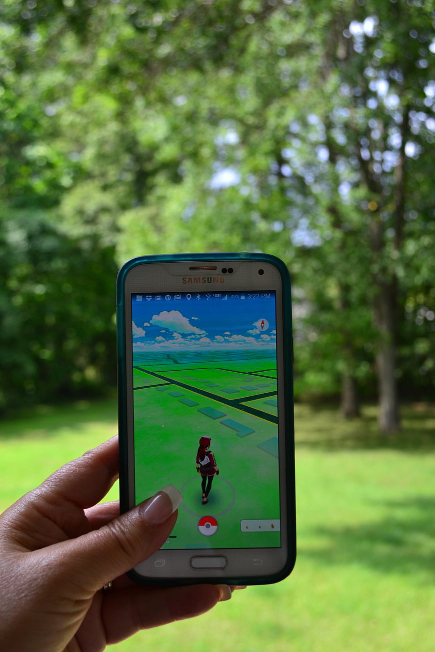 Hand holding smartphone playing Pokemon Go in park