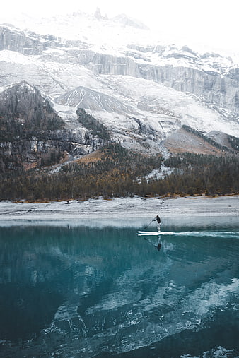 Lone paddleboarder on turquoise lake with snowy mountains