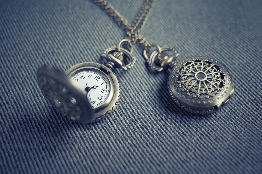 Vintage silver pocket watch and locket on blue denim