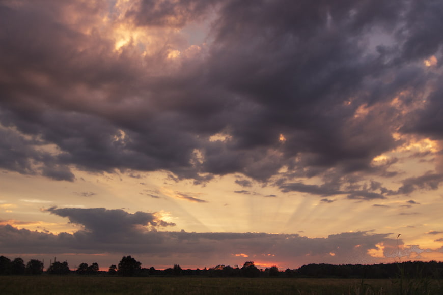 Dramatic sunset sky with golden rays over dark clouds and field