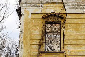 Decaying yellow building facade with cracked wall and broken window
