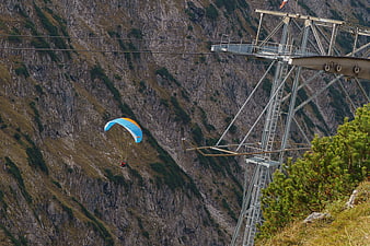Paraglider flying near cable car mast in alpine mountains