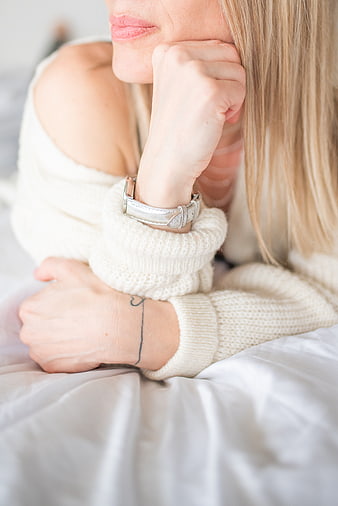 Cozy blonde woman in white sweater lying on bed